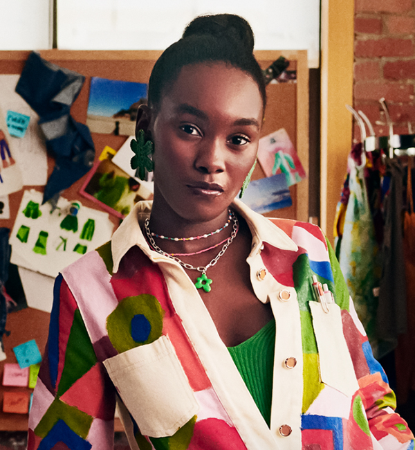 A woman wearing a colorful jacket stands in her studio