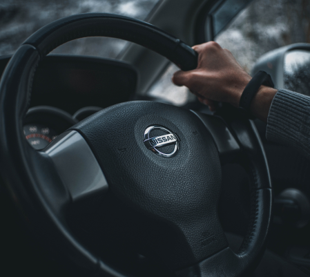A person holding a nissan car steering wheel