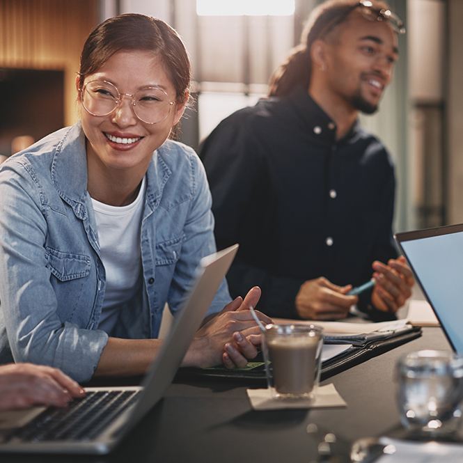 Two employees working together at a desk over their laptops