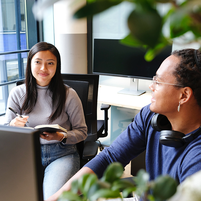 Two employees working together at a desk over their laptops