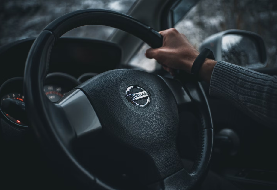 A Nissan car steering wheel with a hand holding it