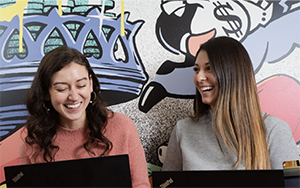 Two people laughing while working on laptops