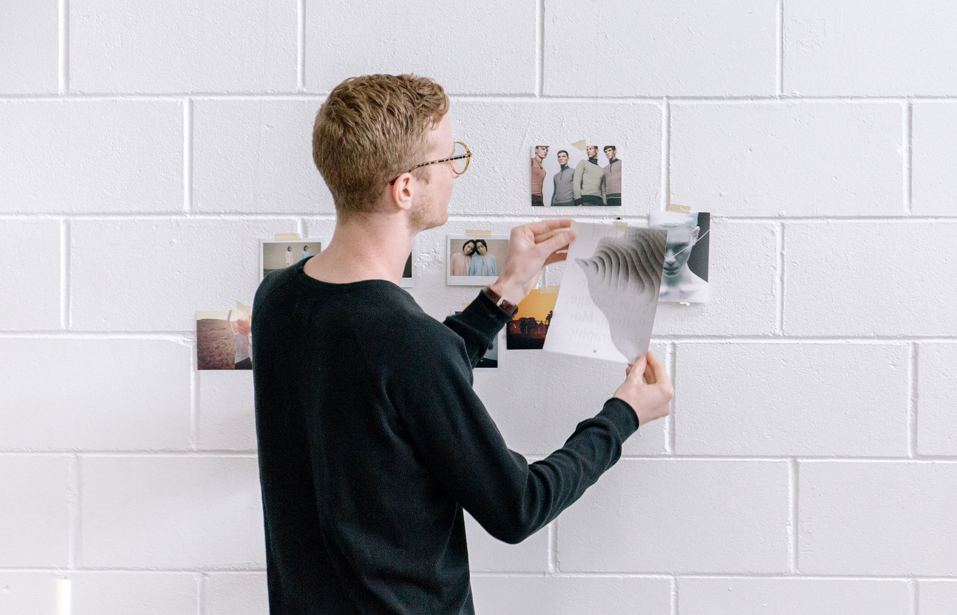 A person adding photos to a white brick wall