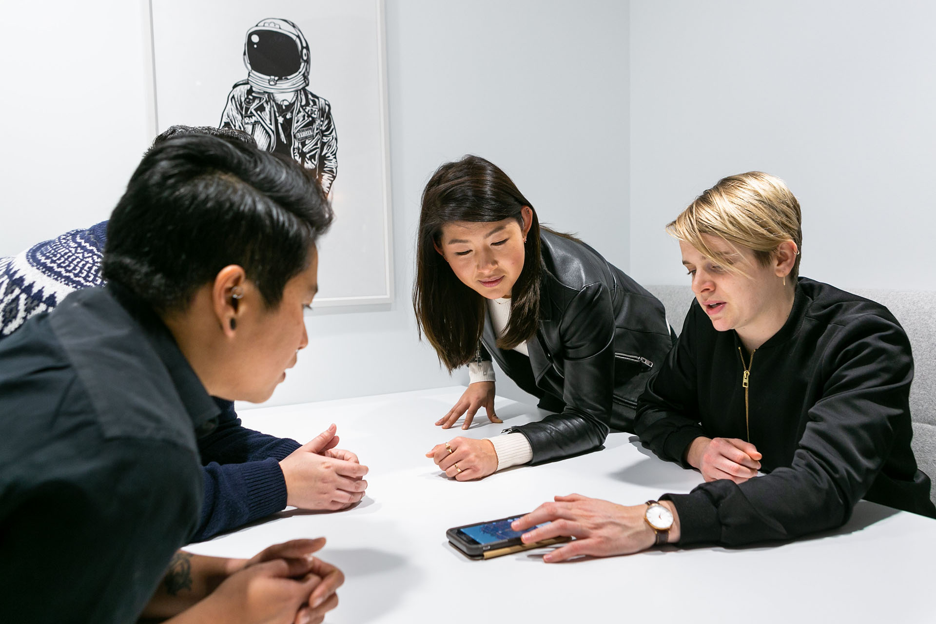 Four employees working over a cellphone at a white table