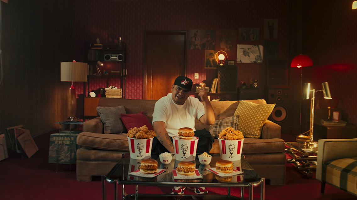 Mexico’s top freestyling artist ‘Aczino’ is sitting in his living room with KFC buckets of chicken and chicken sandwiches in front of him on the table