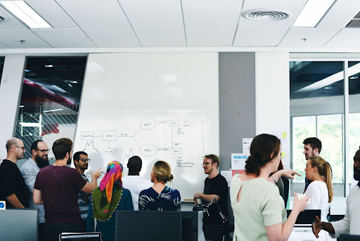 Diverse group of casually dressed people in front of whiteboard with a process drawn on it