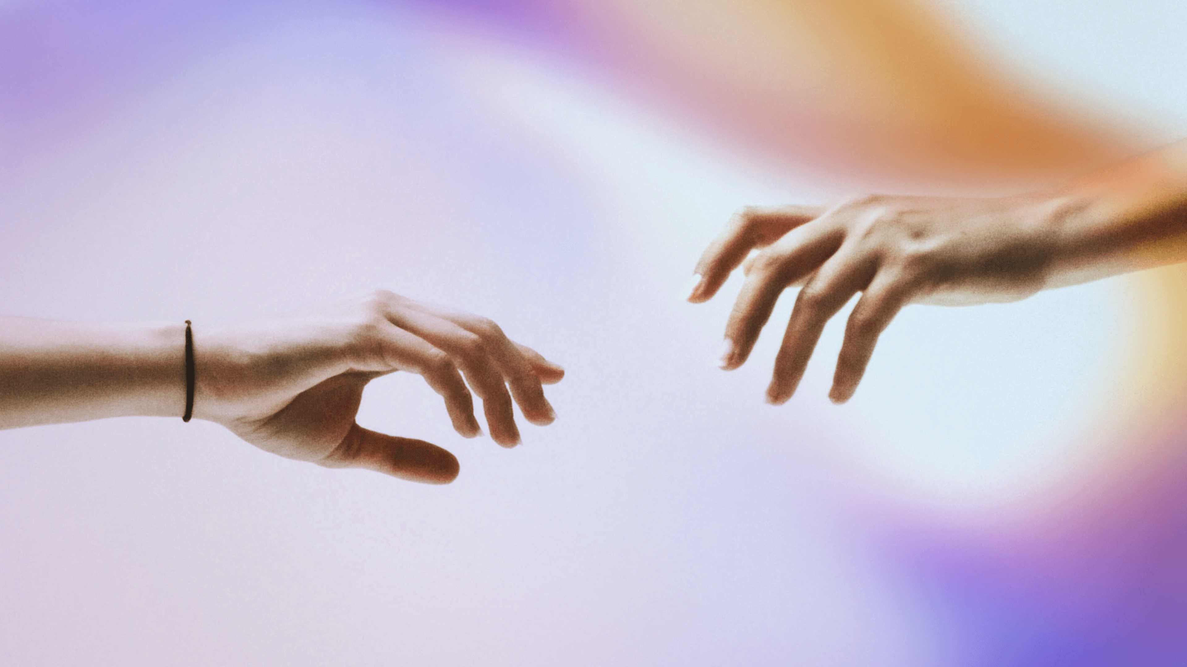 Two hands reaching towards each other with fingers slightly extended, set against a soft, gradient background of purple, blue, and orange hues. One hand has a black wristband.