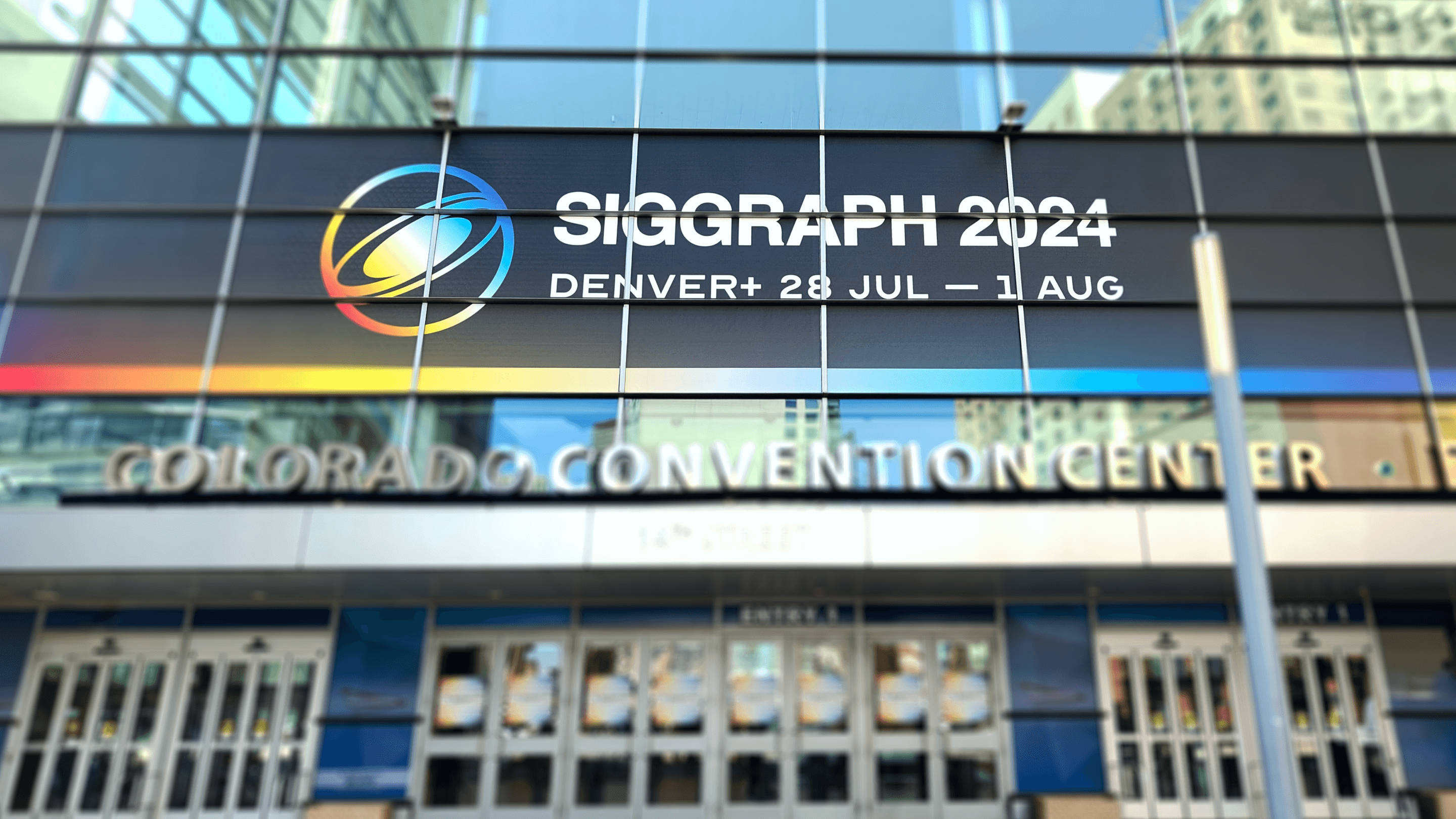 The entrance to the SIGGRAPH conference. A glassy building facade faces the viewer with a large SIGGRAPH sign emblazoned above the doors.