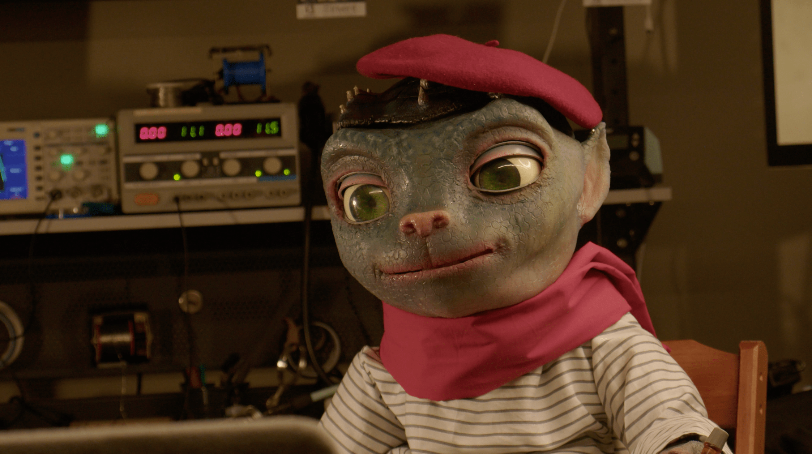 Image of Sir Martian, an animatronic in the form of an alien with large eyes and a cat-like nose. He wears an outfit befitting a Parisian street portrait artist.