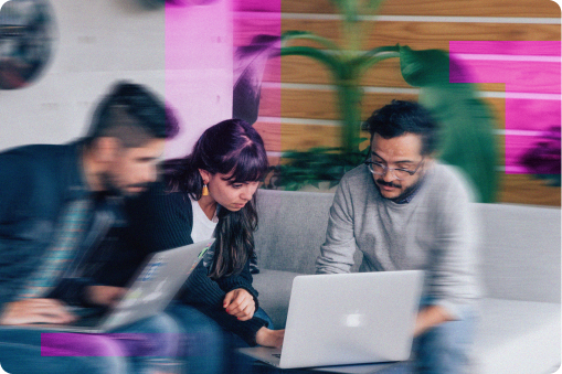 Three people working together in an office surrounding a laptop