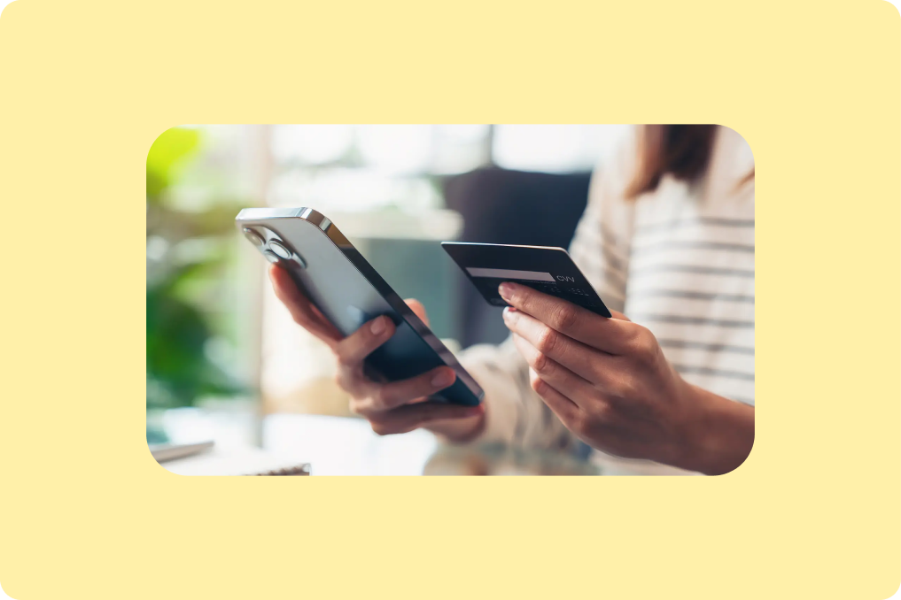 A person looking on their iPhone and holding a credit card making a purchase