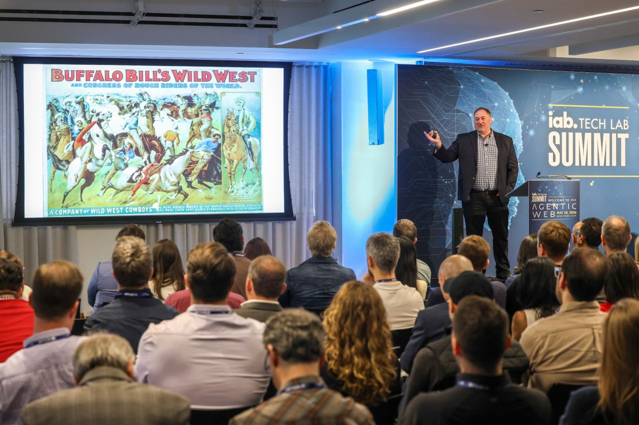 A presenter from the IAB Tech Lab showing a vintage advertisement to a room full of marketing industry leaders.