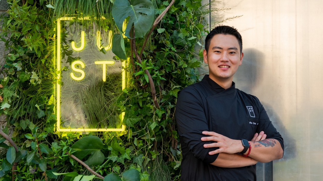 A chef stands in front of the restaurant neon sign covered in plants