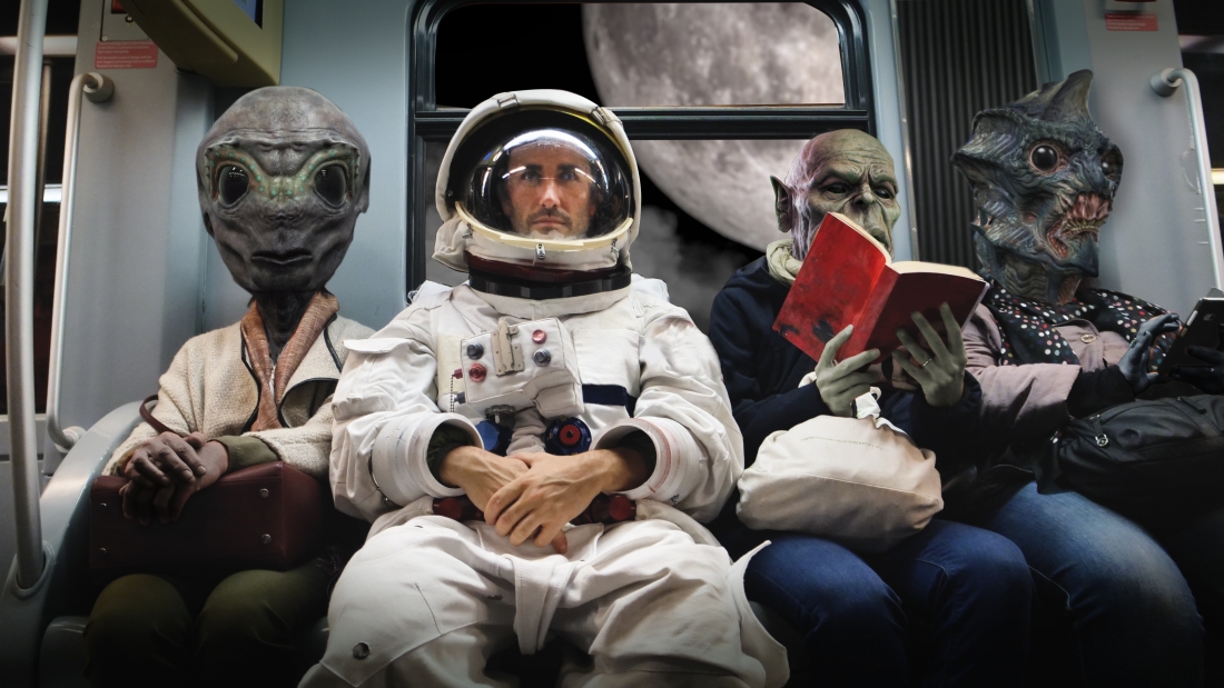A astronaut sitting on a train with aliens next to him