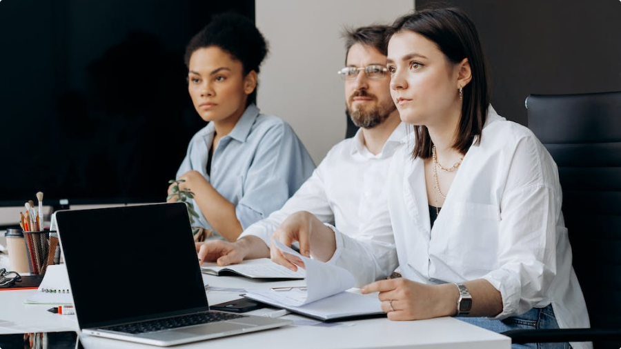 Three employees listening to a presentation with their laptops
