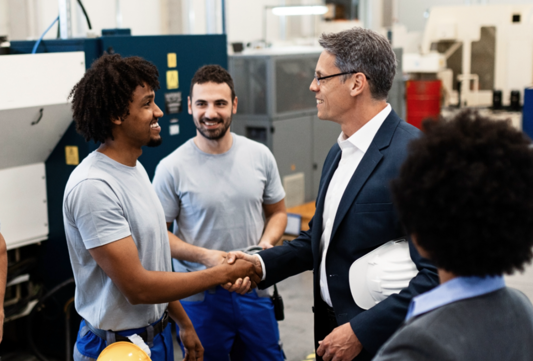 Businessmen shaking hands in a factory. Two factory workers and two people in suits are collaborating.