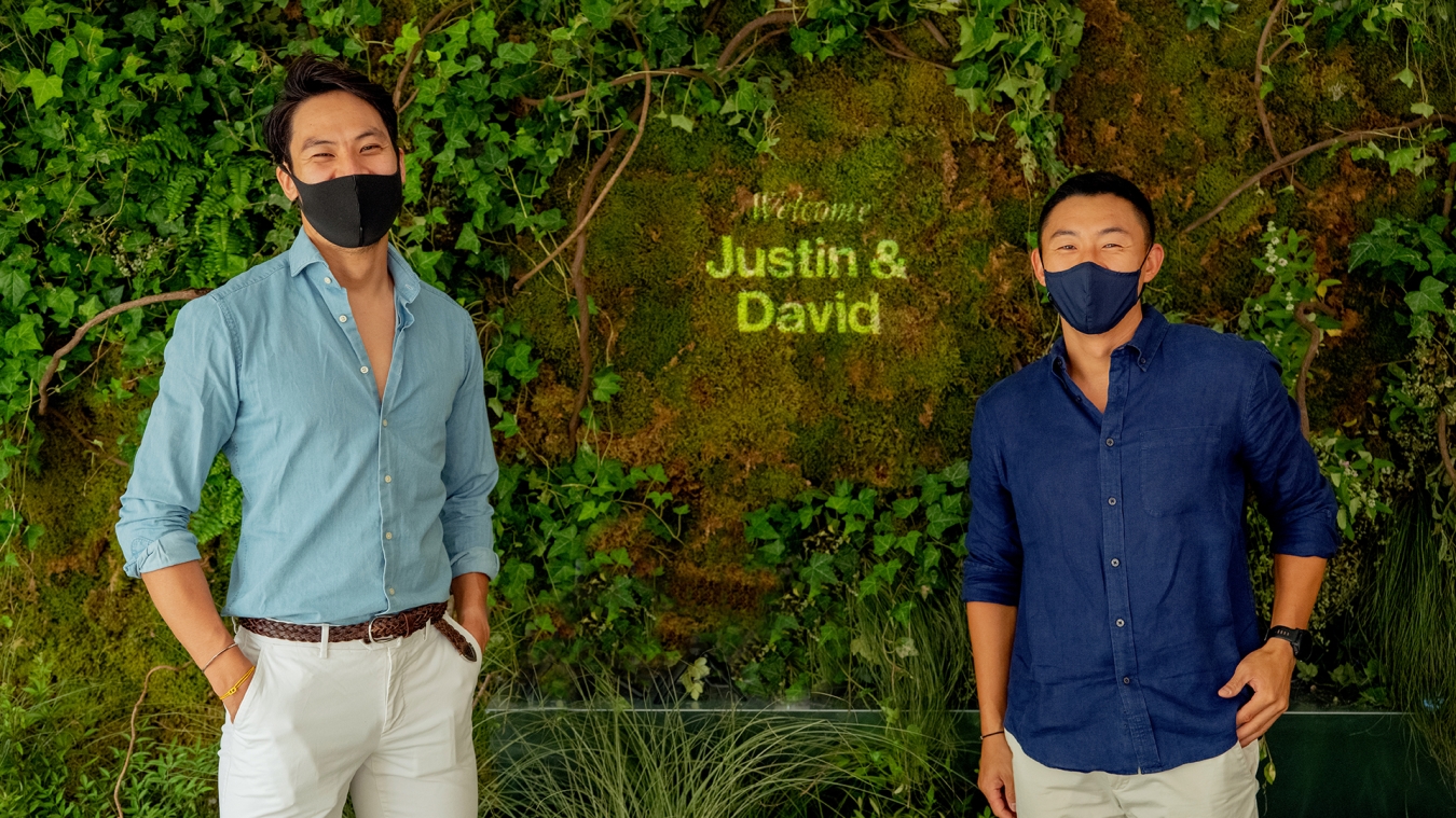 Two people stand in front of a grassy wall with their names shined on it