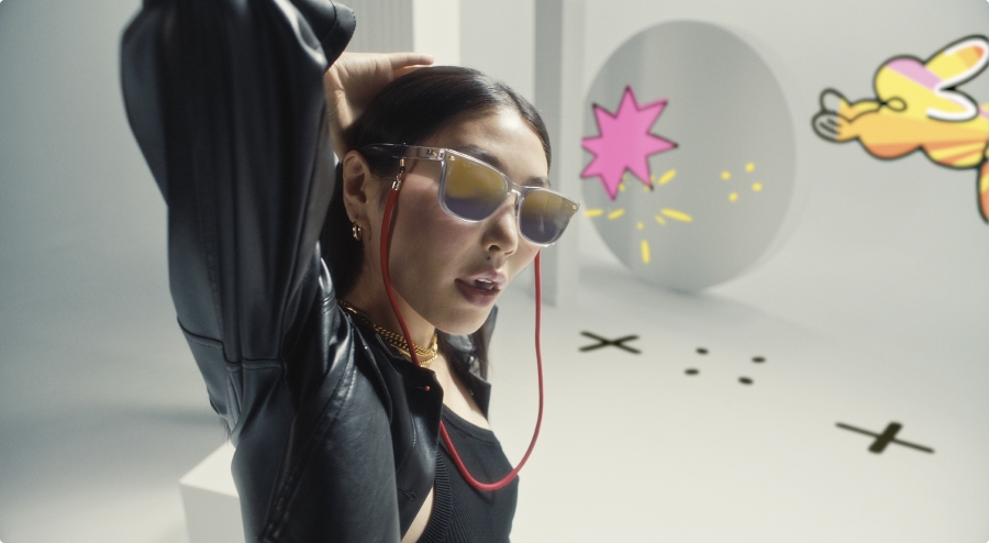 The image features a woman wearing sunglasses and earphones, standing in front of a white background. She is the main focus of the image, positioned towards the center. The woman is also wearing a red cord, which adds a pop of color to her outfit.