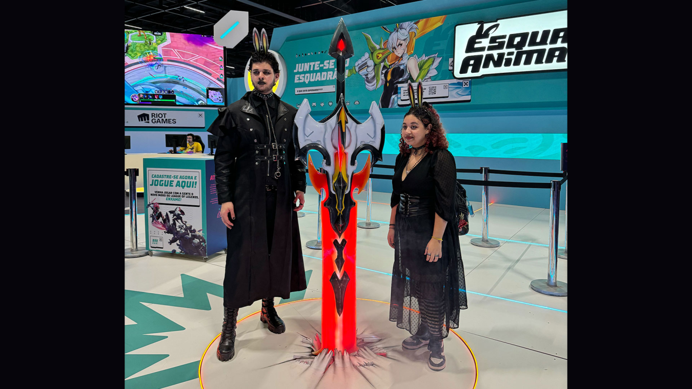 Two people dressed in black clothes posed alongside the League of Legends sword.