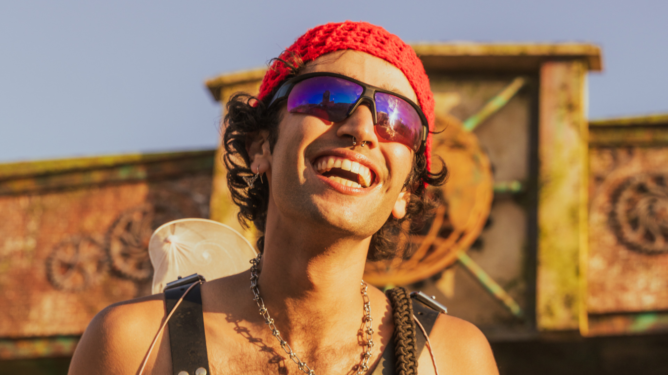 A festival attendee at Boomtown Unboxed smiling in the sun, wearing a red beanie and sunglasses, representing the positive and unique experiences created by AI-powered personalization.