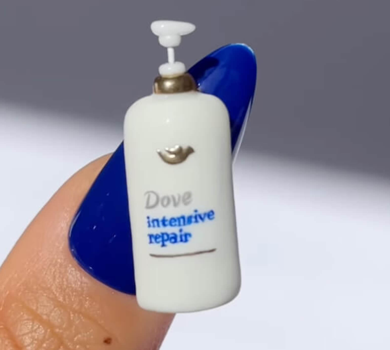 A Dove Hair product made into a miniature that is attached to a set of nails with a life-sized version behind it.