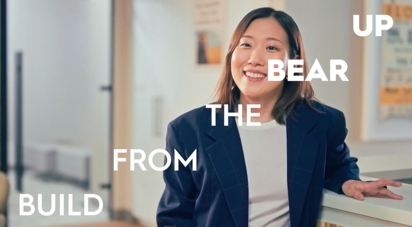 A financial analyst smiling in an office with the words "Build From The Bear Up" written on the image.