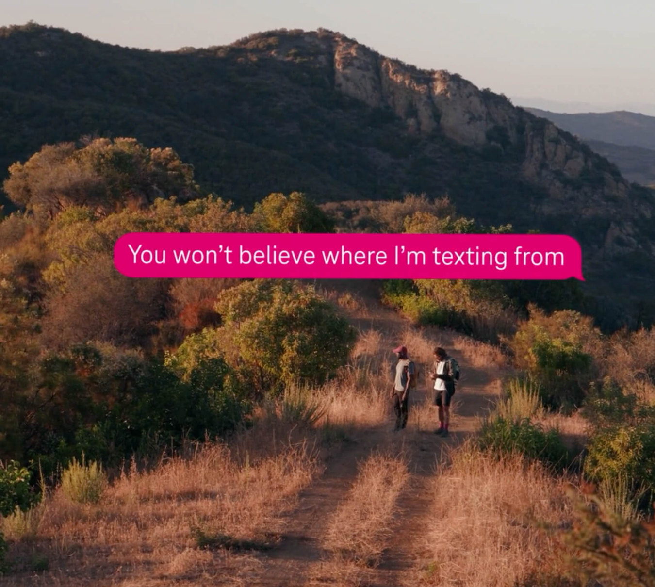 Two people standing out in the mountains with a text bubble that says "You won't believe where I'm texting from" on top of the image.