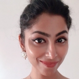 portrait of a woman with dark hair in a bun, eyeliner and an earring, against a white background