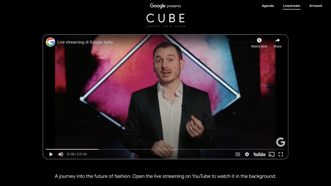 The image shows a man in a suit standing in front of a screen. The man is the focal point of the image, as he is positioned prominently in the center. The screen is large and occupies a significant portion of the image.  On the screen, there is text that reads "Google presents", indicating that this is a presentation or event organized by Google. Adjacent to the main text, there are several smaller texts that read "Agenda", "Livestream", and "Artwork", likely indicating different sections or features of the