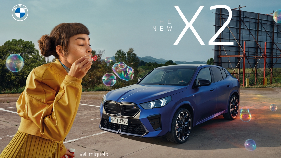 BMW The new X2 car in blue seen from the front. In front of the car you see Lil Miquela dressed in a yellow skirt and a yellow jacket. She is blowing bubbles