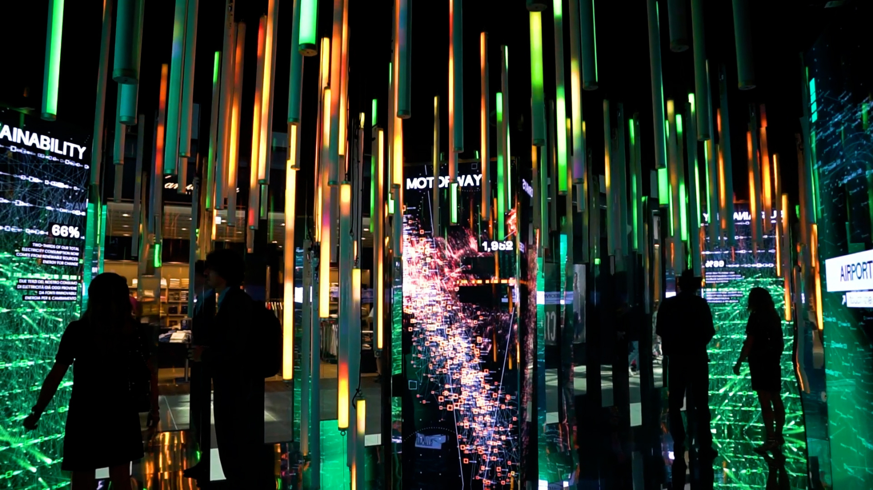 A dark image with a lot of vertical lights in the colors green and yellow. All mirror wall reflecting the lights and screens.