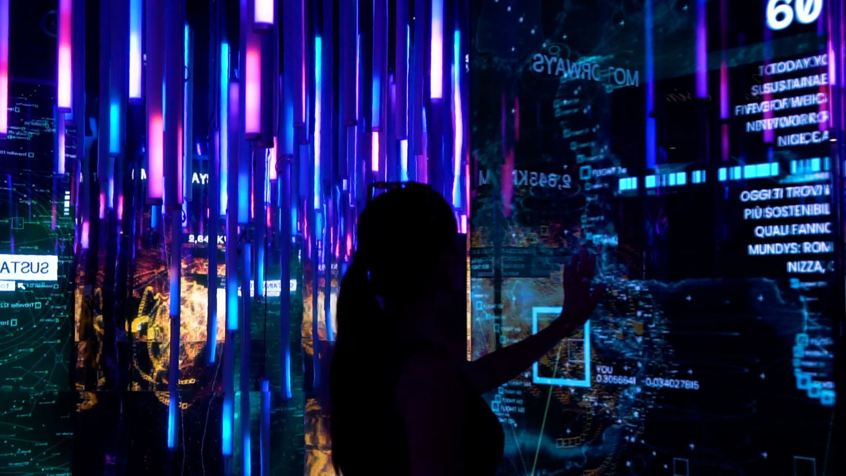 A dark image with a lot of vertical lights in the colors purple and blue. All mirror wall reflecting the lights and screens. A silhouette of a person standing in front of a screen touching the screen.