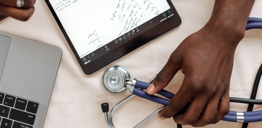A stethoscope, laptop, and iPad are hovered over by a person