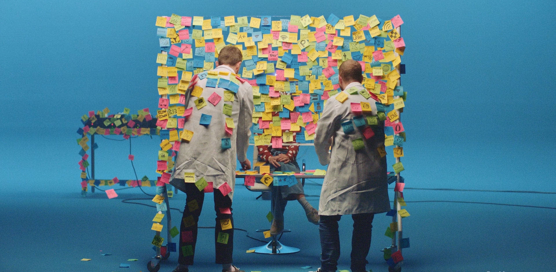 Two people putting post-it notes all over a wall