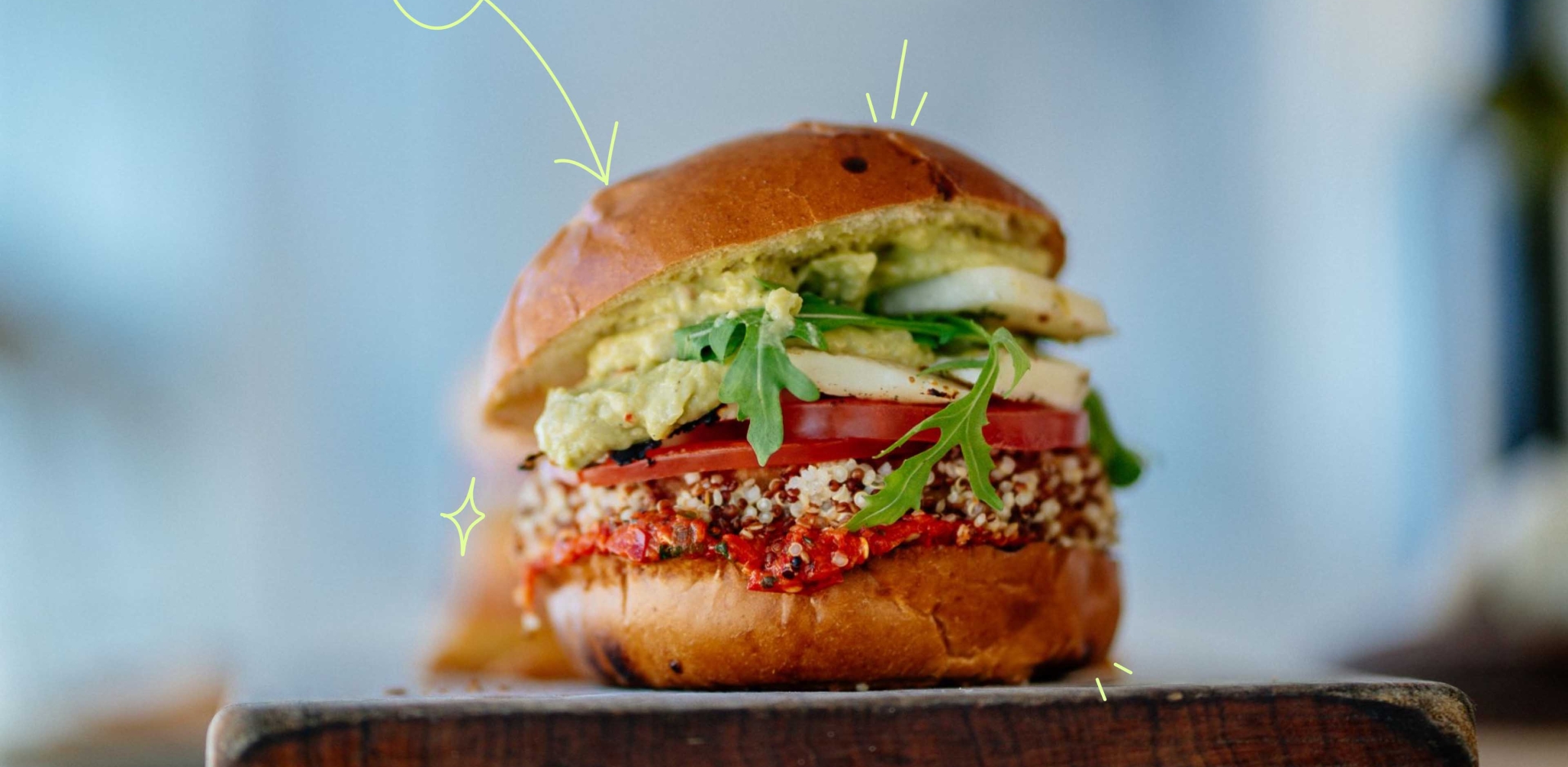 A plant based burger sitting on a table with leafy greens and veggies