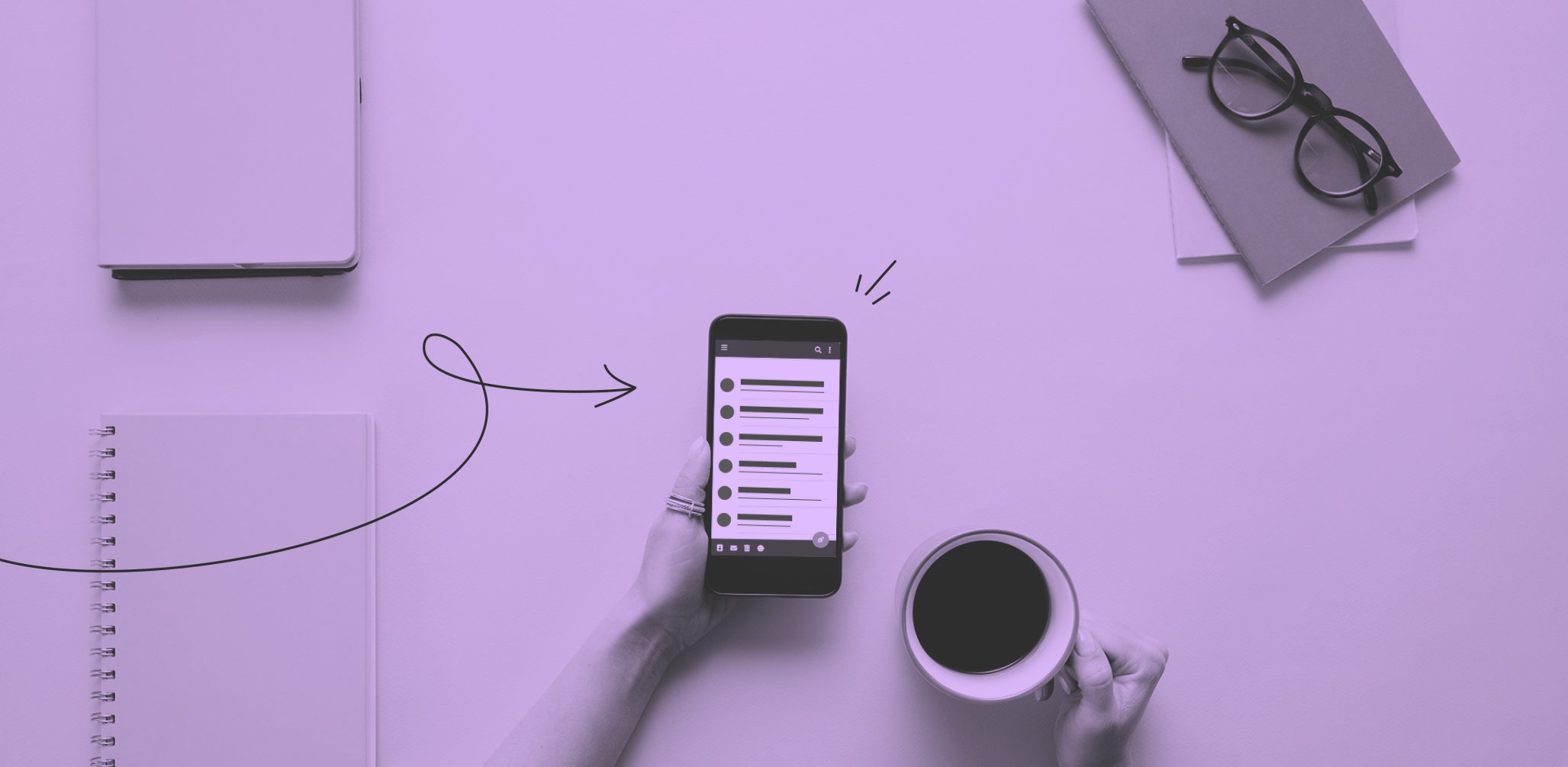An arm holding a iphone sitting at a table with a notebook and coffee