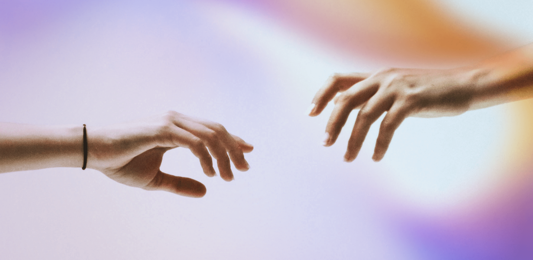 Two hands reaching towards each other with fingers slightly extended, set against a soft, gradient background of purple, blue, and orange hues. One hand has a black wristband.
