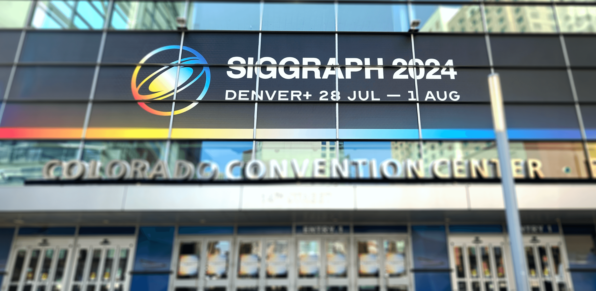 The entrance to the SIGGRAPH conference. A glassy building facade faces the viewer with a large SIGGRAPH sign emblazoned above the doors.