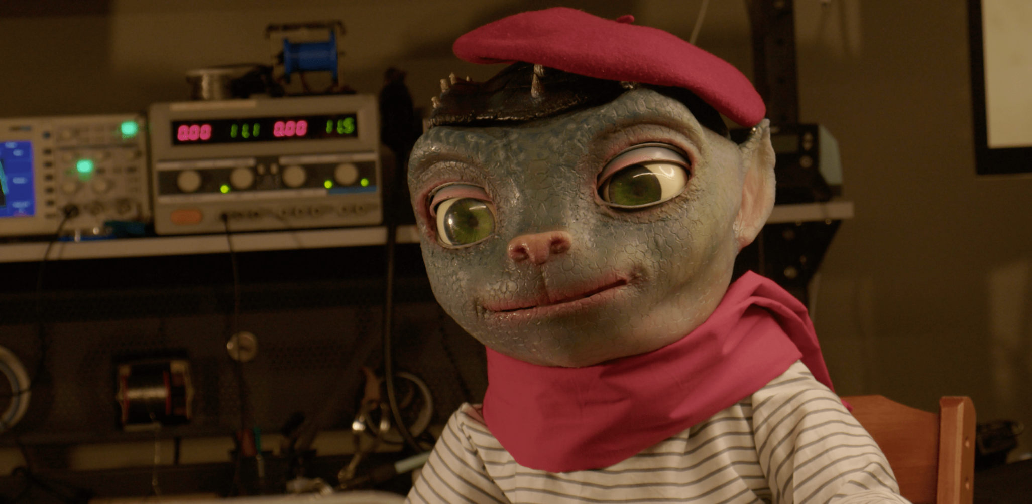 Image of Sir Martian, an animatronic in the form of an alien with large eyes and a cat-like nose. He wears an outfit befitting a Parisian street portrait artist.