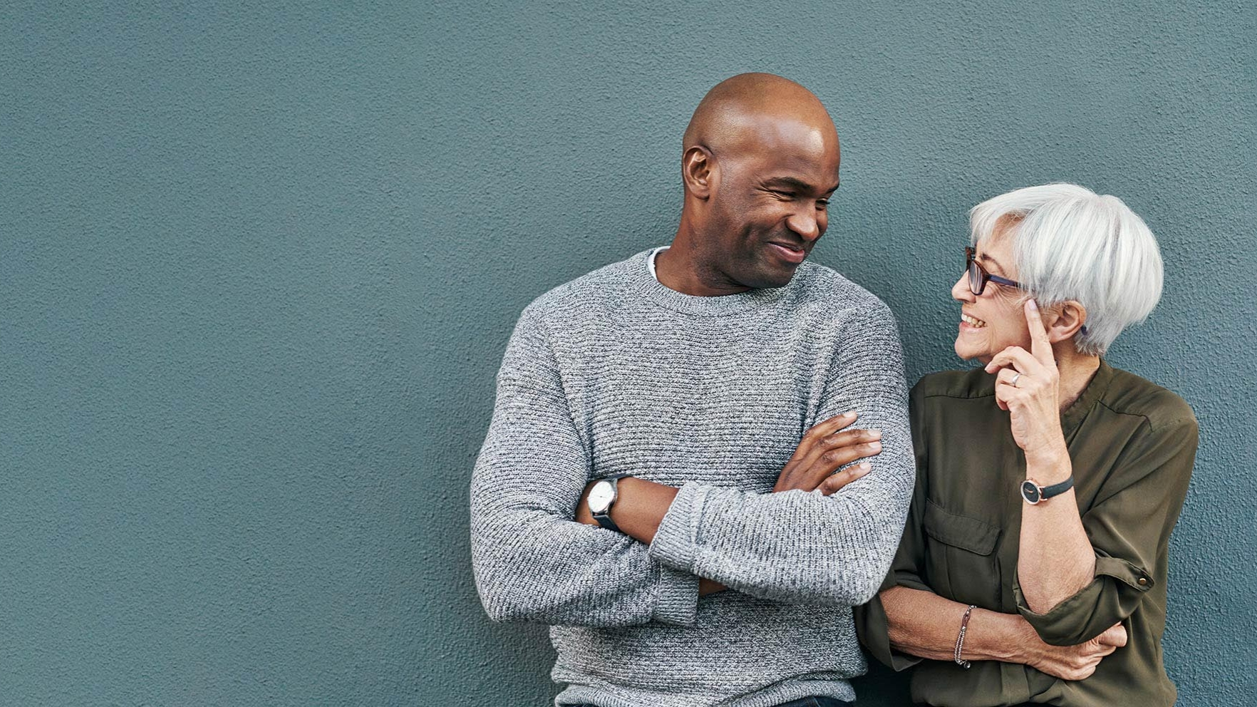 A man and woman stand next to each other talking up against a wall