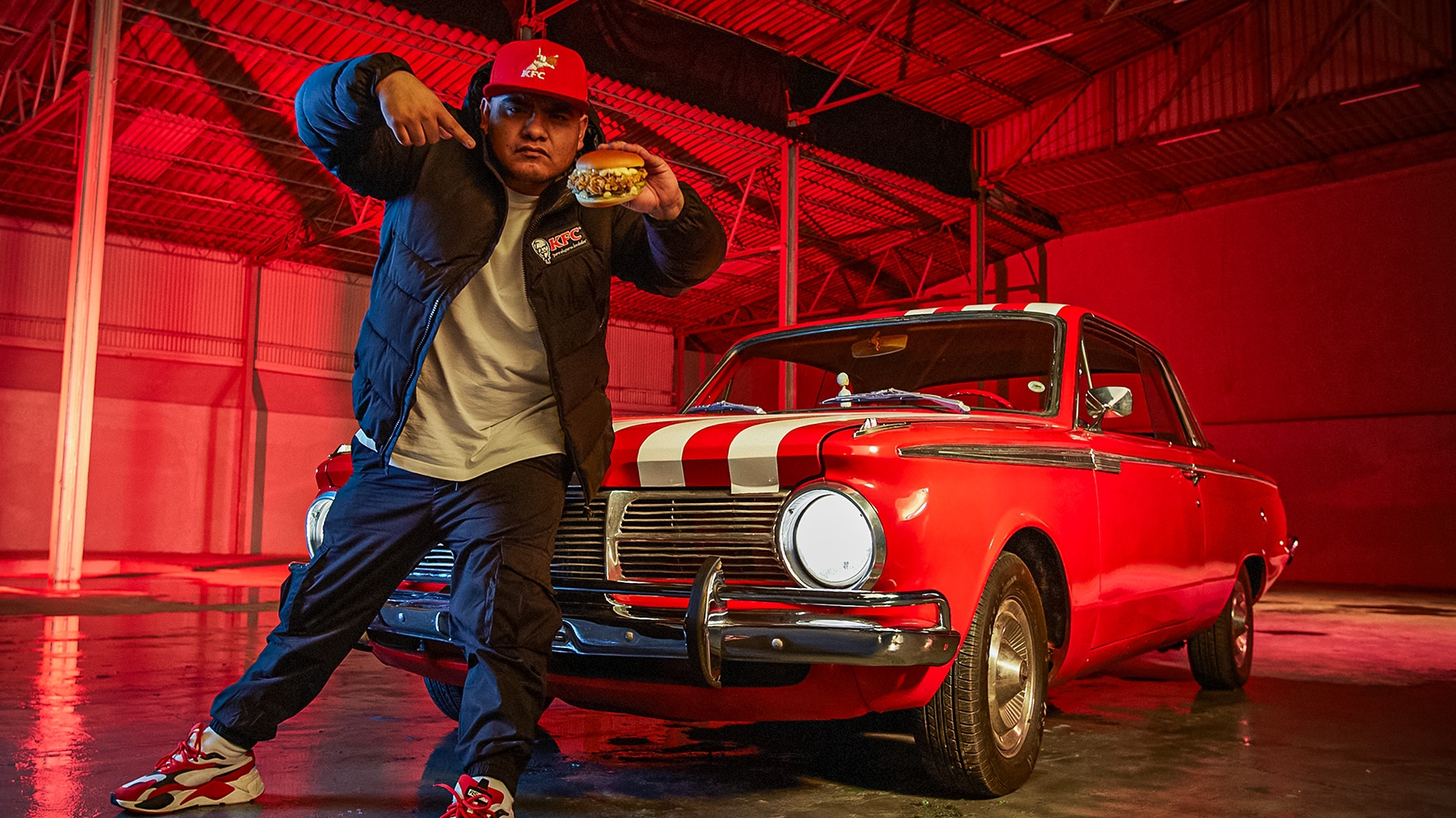 Aczino rapping in front of a red car holding a chicken sandwich