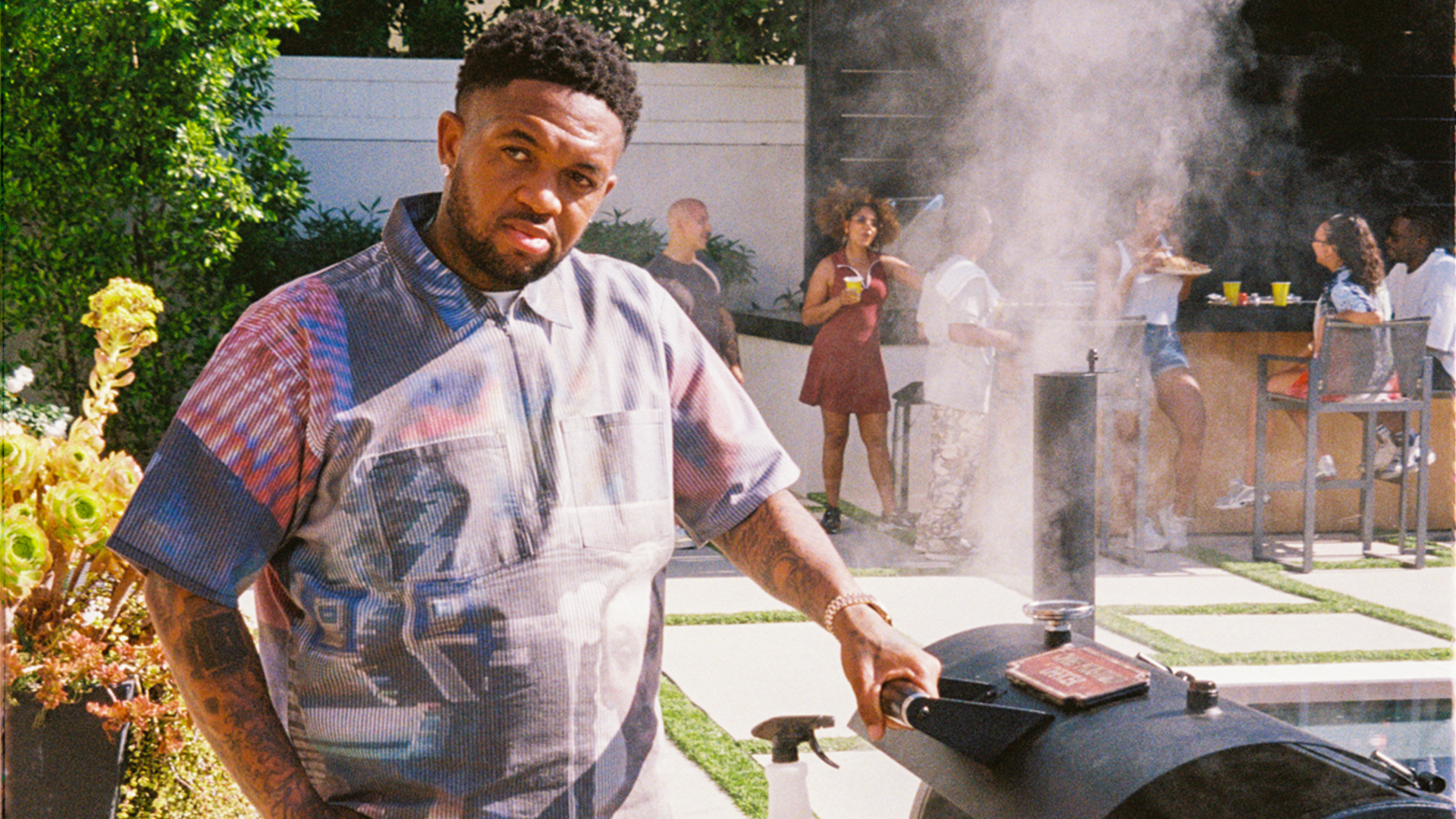 Music producer DJ Mustard grilling outdoors at a luxurious summer party, promoting the new Heinz Mustaaaaard product collaboration with a backyard BBQ lifestyle feel.