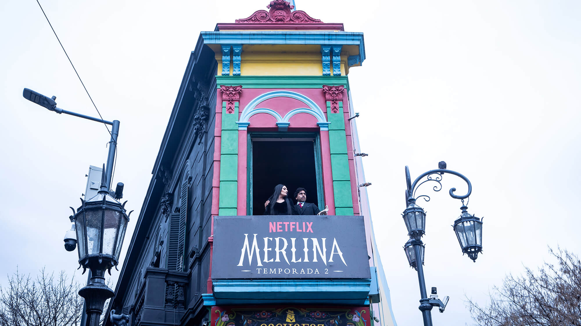 Actors portraying Gomez and Morticia Addams standing on a balcony in Caminito, Argentina during the "Darkminito" activation for Netflix.