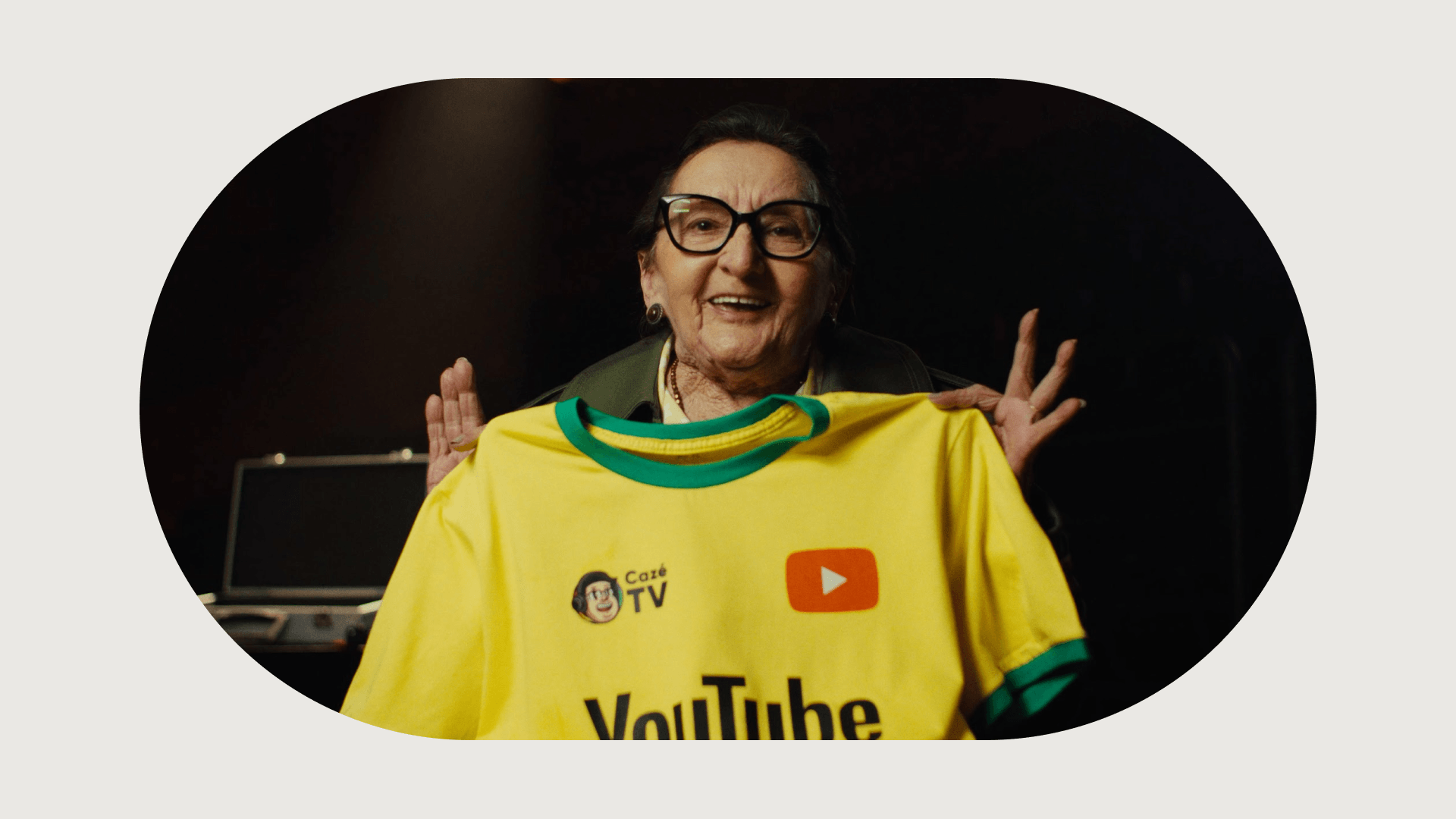 Brazilian actress Tania Maria smiling and holding up a yellow soccer jersey featuring the Cazé TV and YouTube logos.