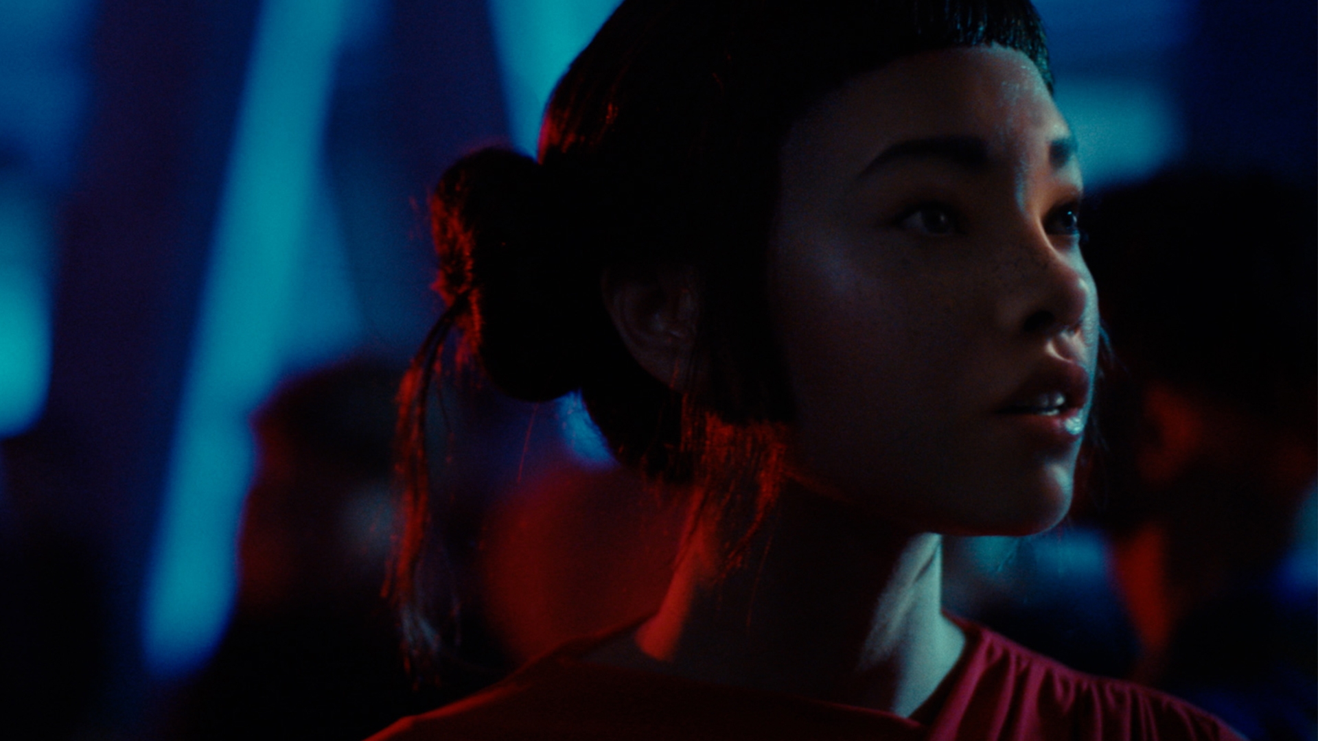 Close up of Lil Miquela. Her face is illuminated by different colored lights. She is looking around with a surprised expression on her face.
