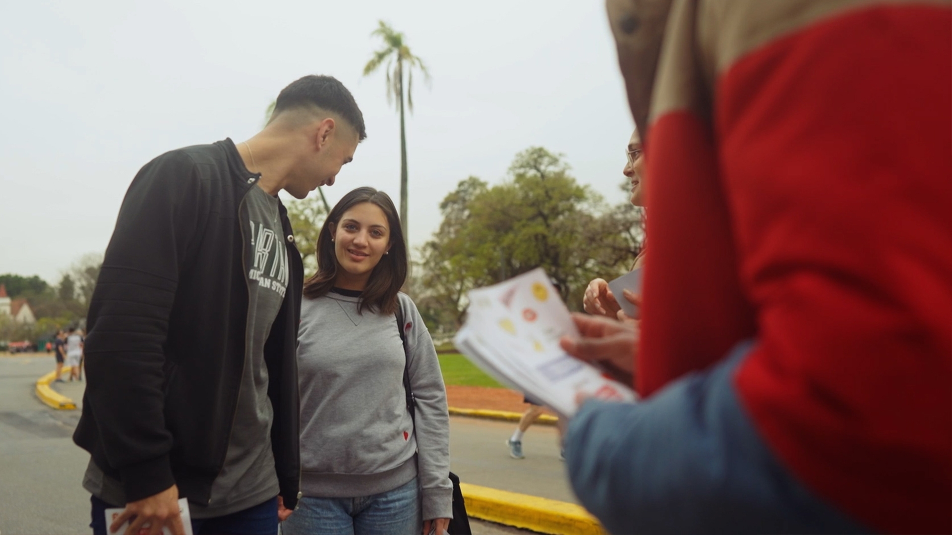 Boy and a girl standing next to eachother listening to somebody who holds folders about save sex.