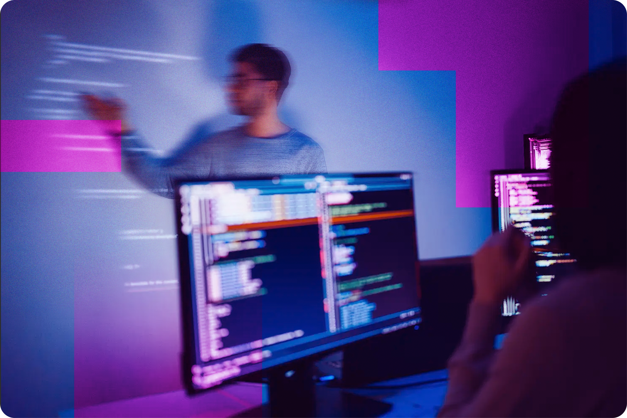 A person working at a dry erase wall while another person codes on a computer