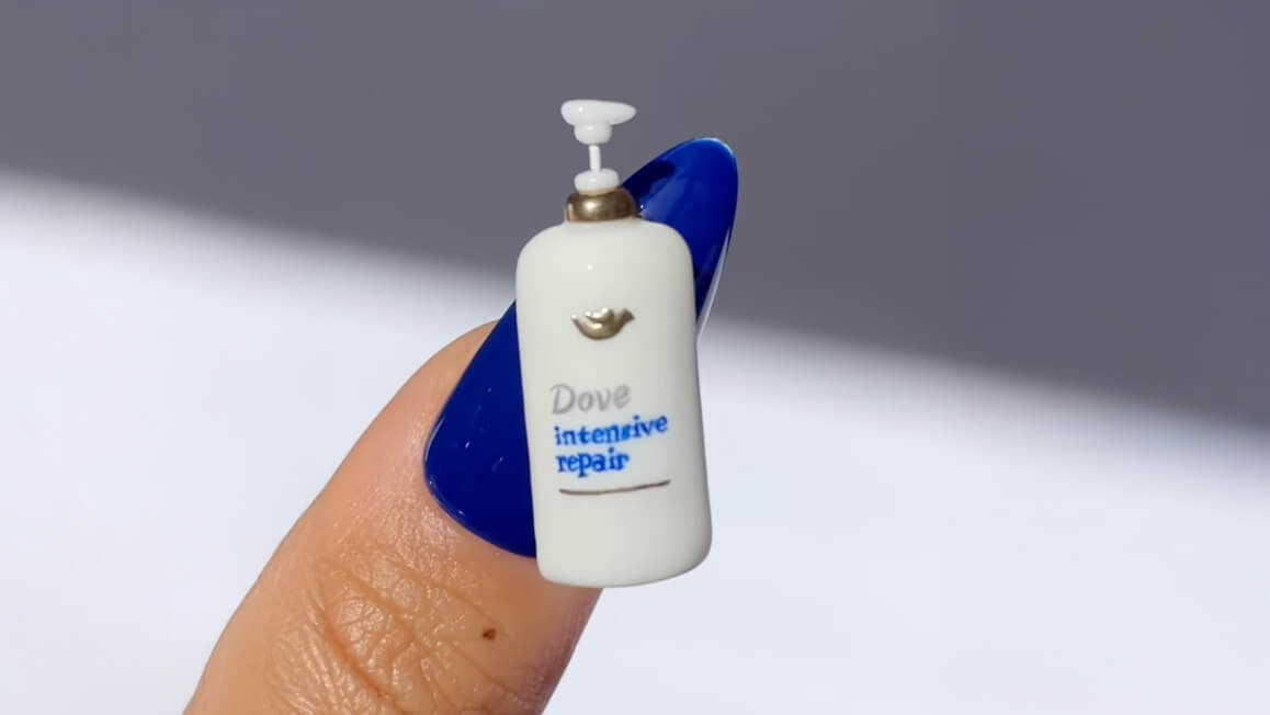 closeup on a woman's fingernail with a miniature of a Dove hair care product attached