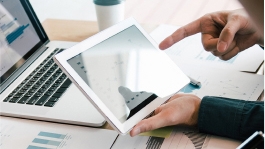 hands holding a tablet in front of a laptop