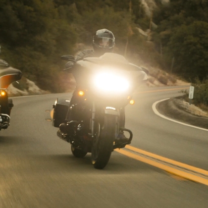Two people riding Harley Davidson motorcycles down the road